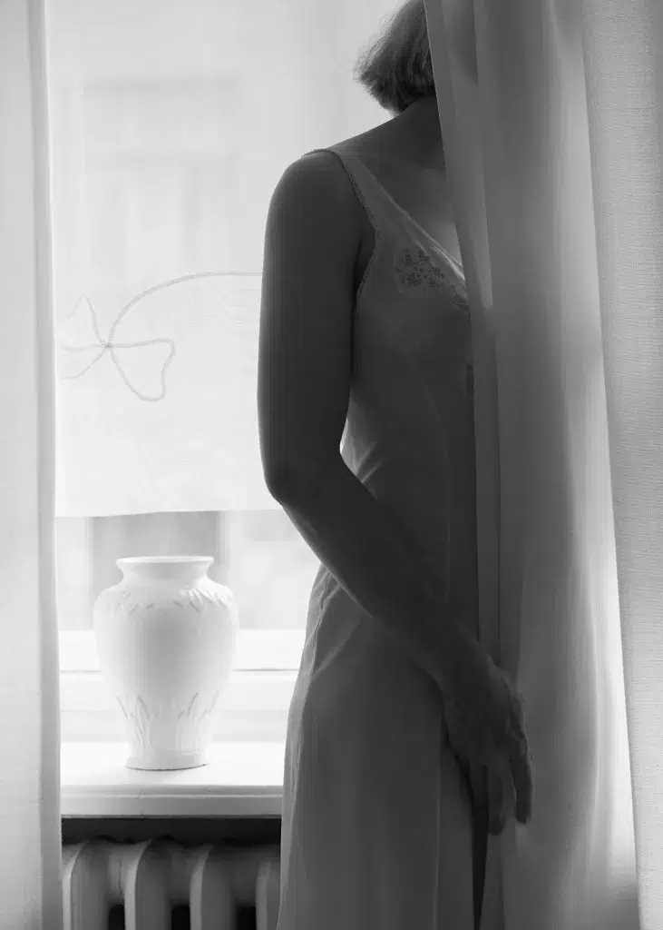 black and white photograph of woman standing by the window